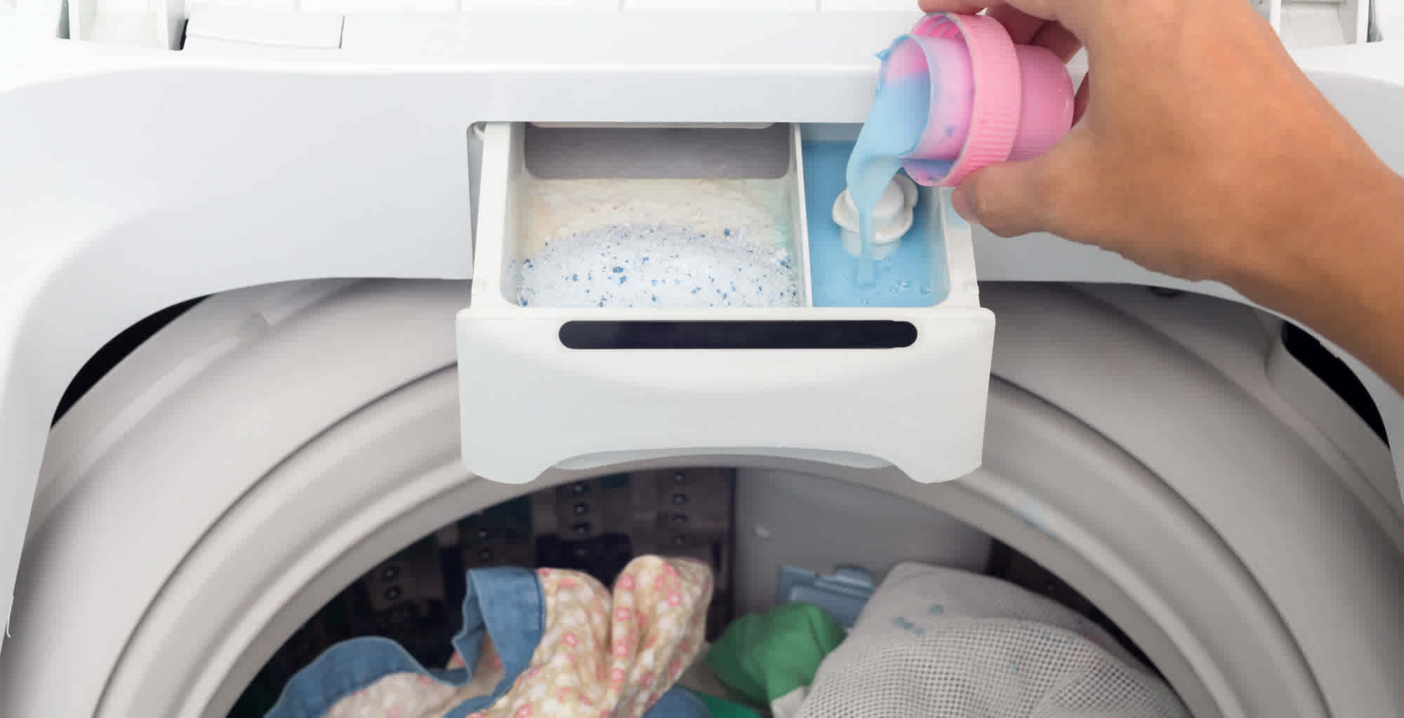 Una mano agregando suavizante al compartimiento correspondiente de la lavadora.