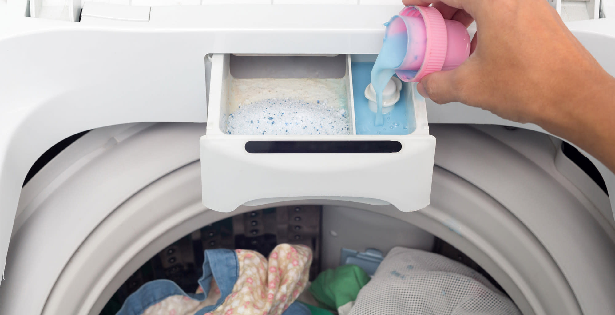 Una mano agregando suavizante al compartimiento correspondiente de la lavadora.