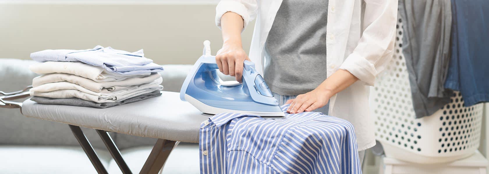 Una pila de camisas planchadas apiladas junto a una plancha y una camisa a rayas arrugada.