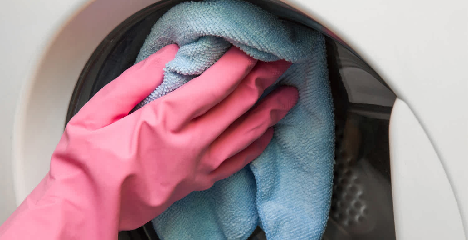 Una-mano-con-guantes-rosas-pasando-un-trapo-por-una-lavadora
