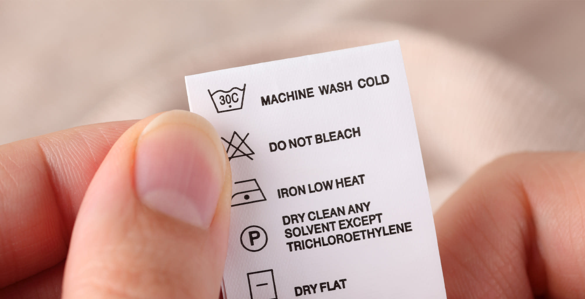 Detalle de unas manos revisando la etiqueta de cuidados de una prenda.