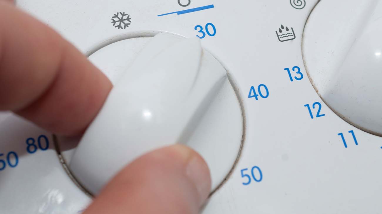 Un hombre seleccionando un programa de lavado frío en una lavadora.
