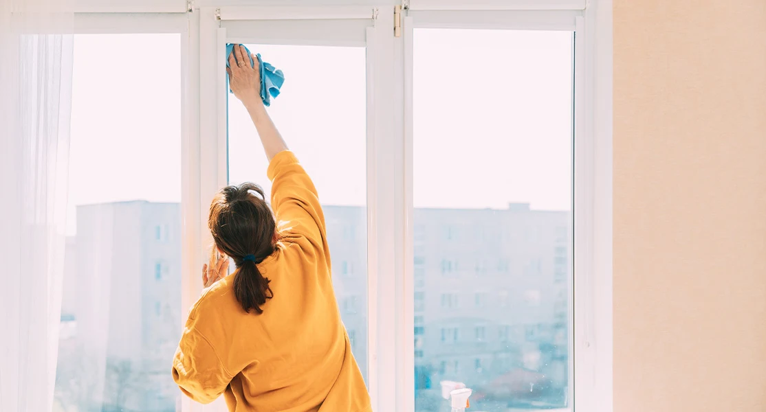 Una mujer limpiando ventanas de vidrio con un trapo azul en un apartamento.