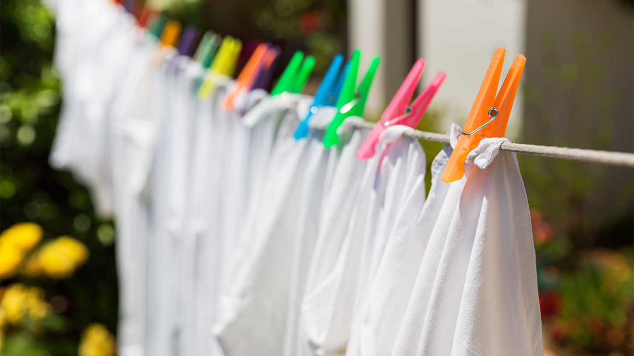 Ropa blanca tendida con broches de colores en un jardín.