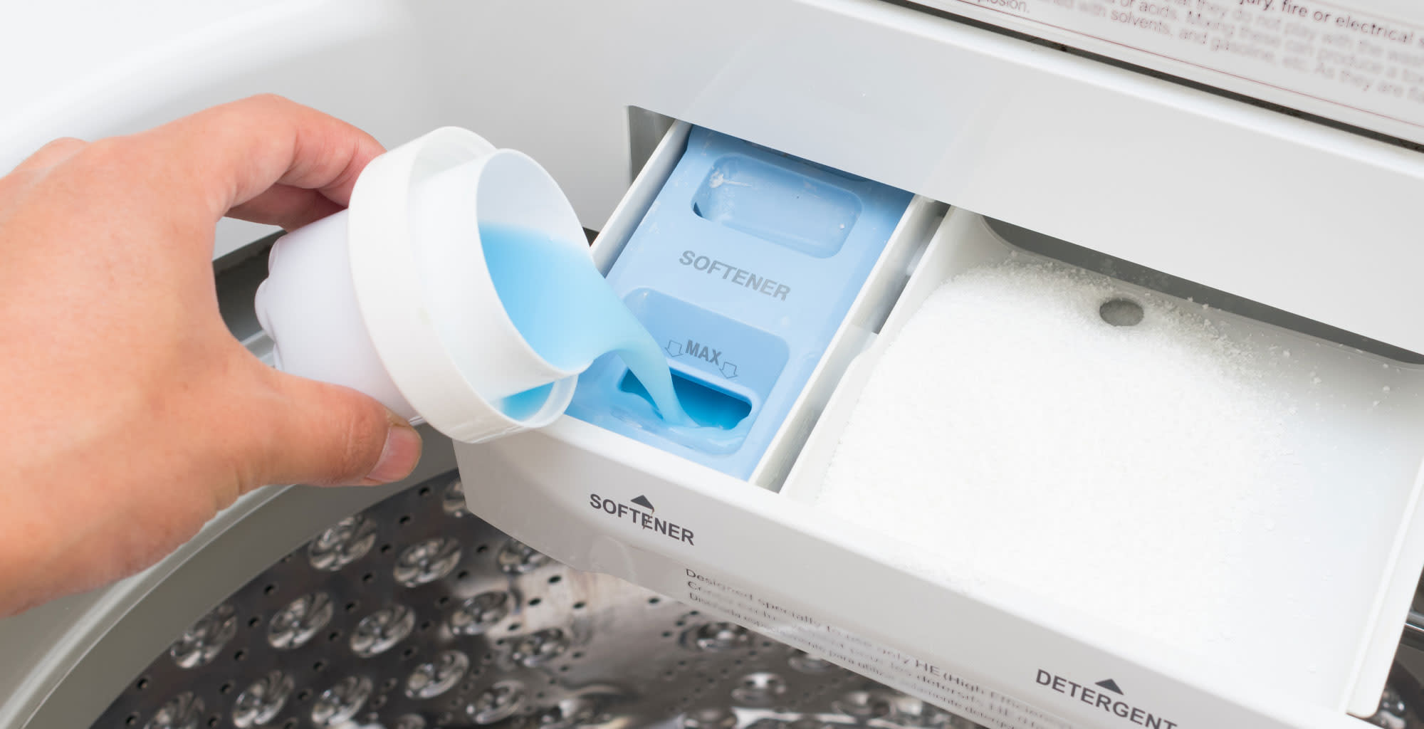 Una mano agregando suavizante en el compartimiento de la lavadora