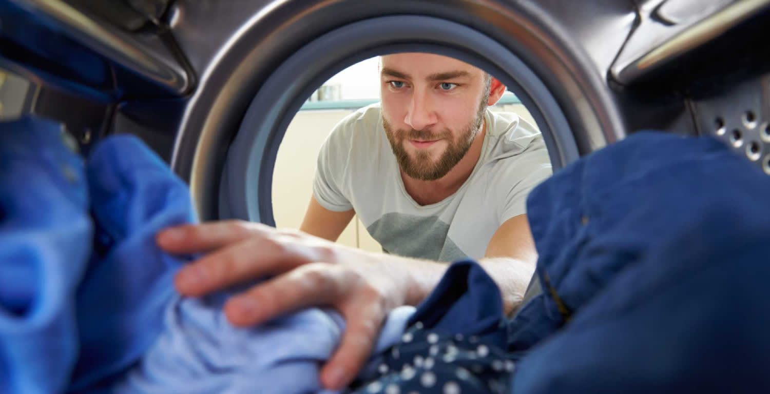 Un hombre ordenando ropa adentro del lavarropas visto desde adentro