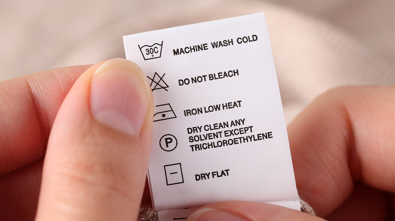 Detalle de unas manos revisando la etiqueta de cuidados de una prenda.
