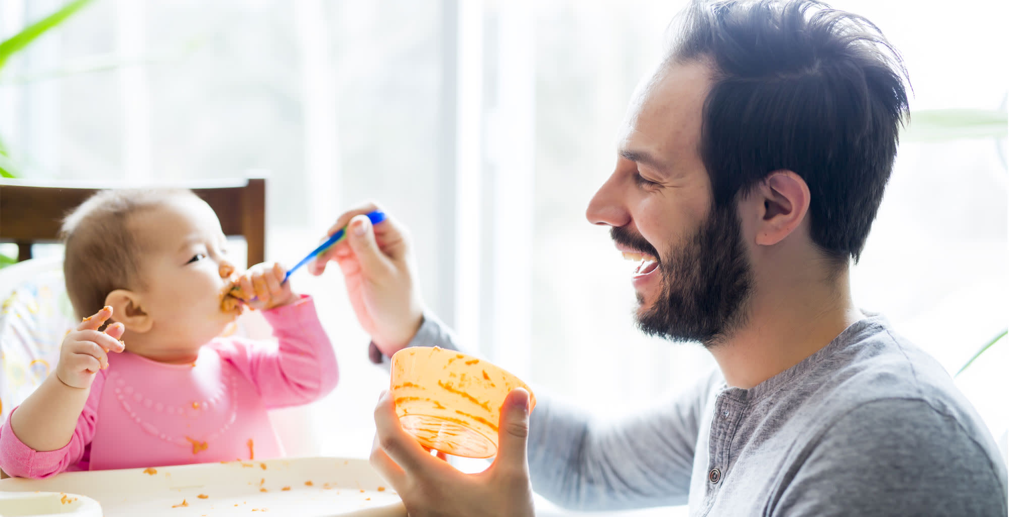 Un hombre alimentando a su bebé que se manchó con la comida.