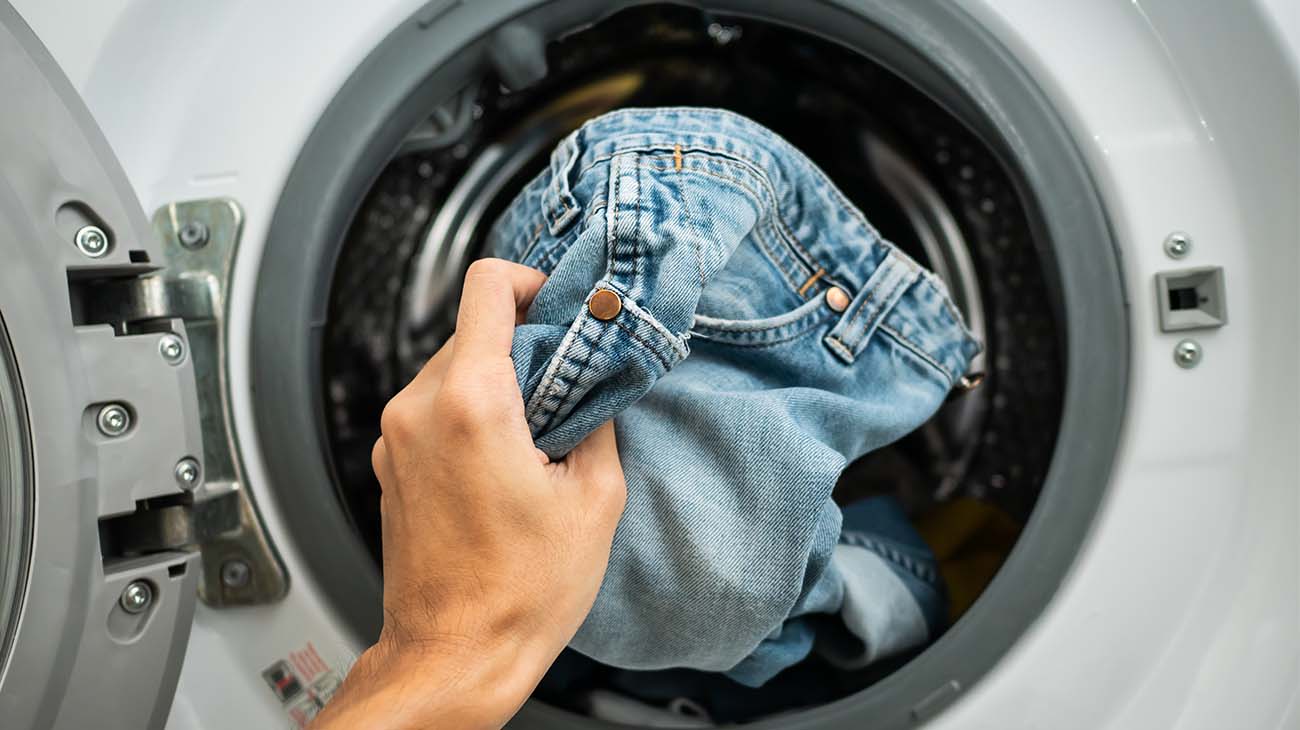 Una mano poniendo jeans dentro de la lavadora