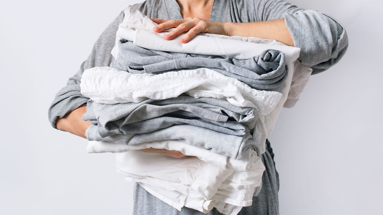 Una mujer sosteniendo una pila de ropa de diferentes colores.