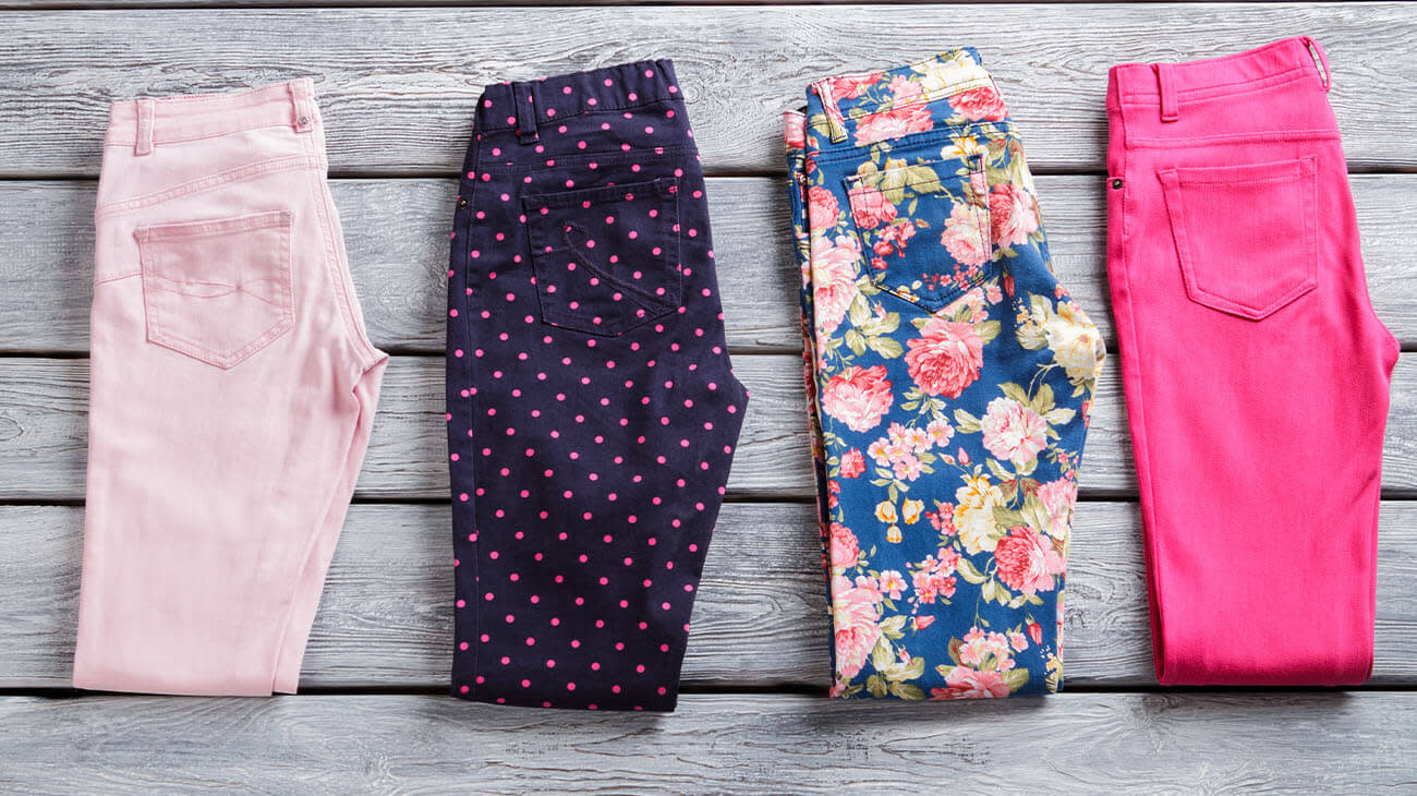 Cuatro pantalones coloridos doblados por la mitad sobre un fondo de madera gris.