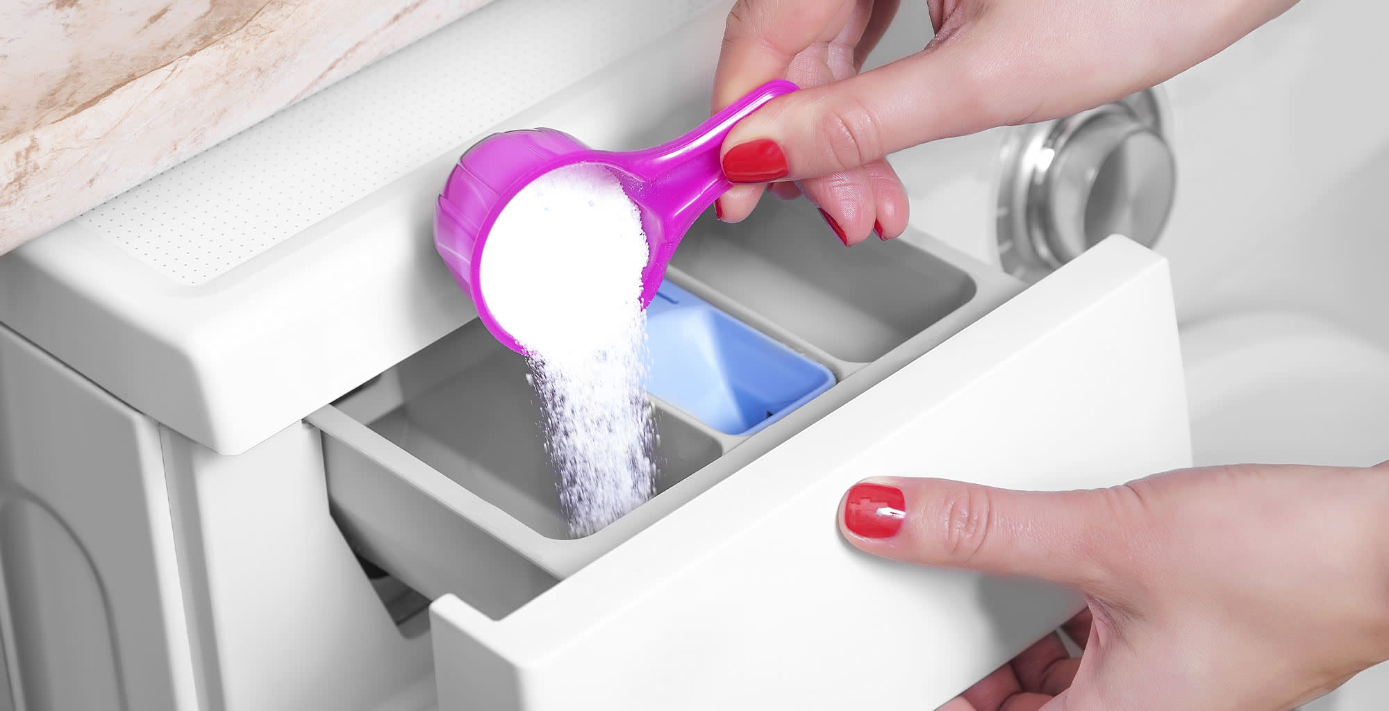 Manos femeninas agregando detergente en polvo en el compartimiento de la lavadora