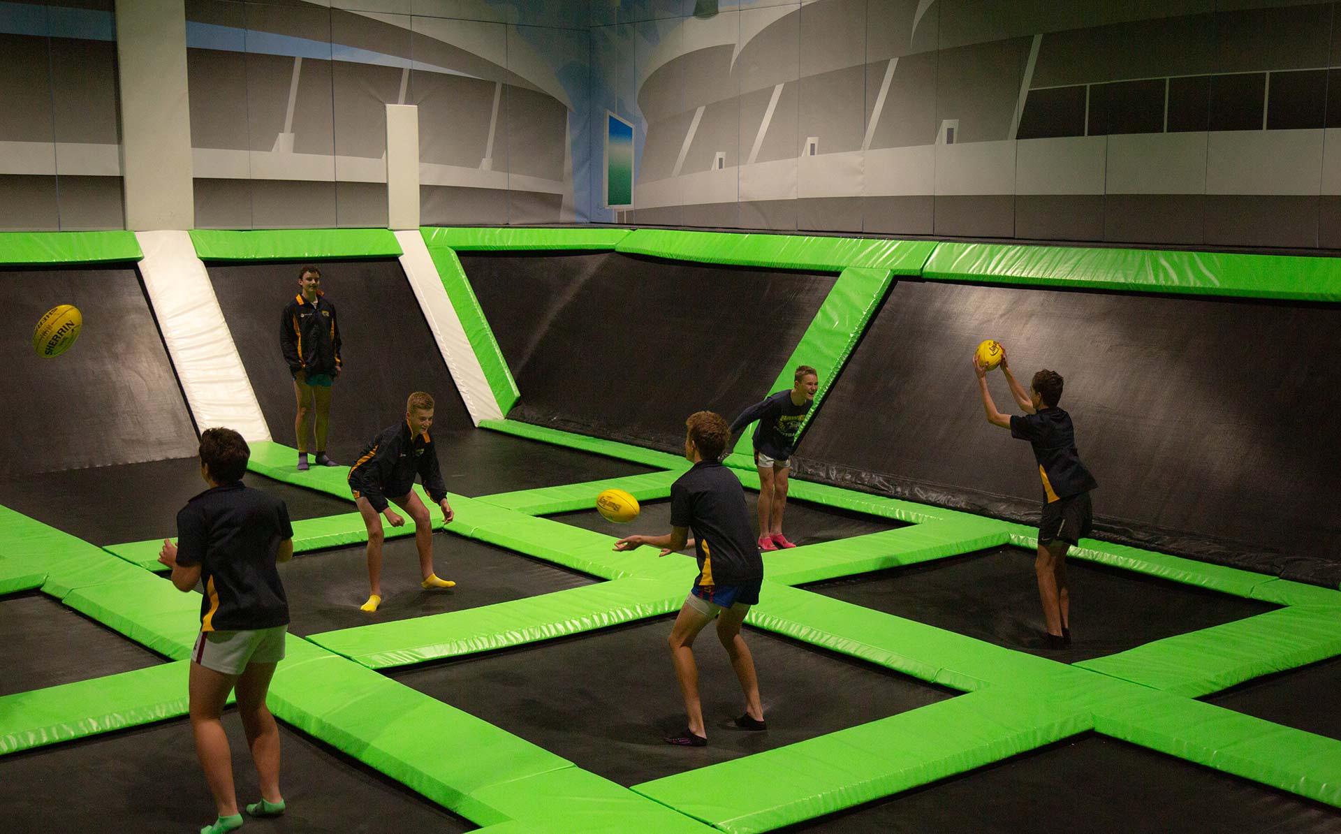 Group of kids are passing footy to each other on a big trampoline