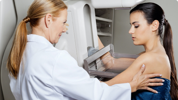 Female doctor assisting female patient undergoing mammogram.