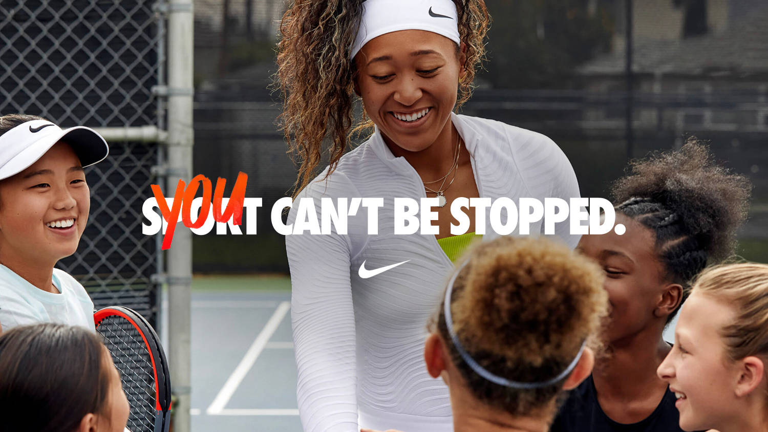 A smiling tennis player in a white Nike outfit stands with a group of diverse kids on a tennis court. Overlaid bold text reads, YOU CAN’T BE STOPPED, with YOU highlighted in red.