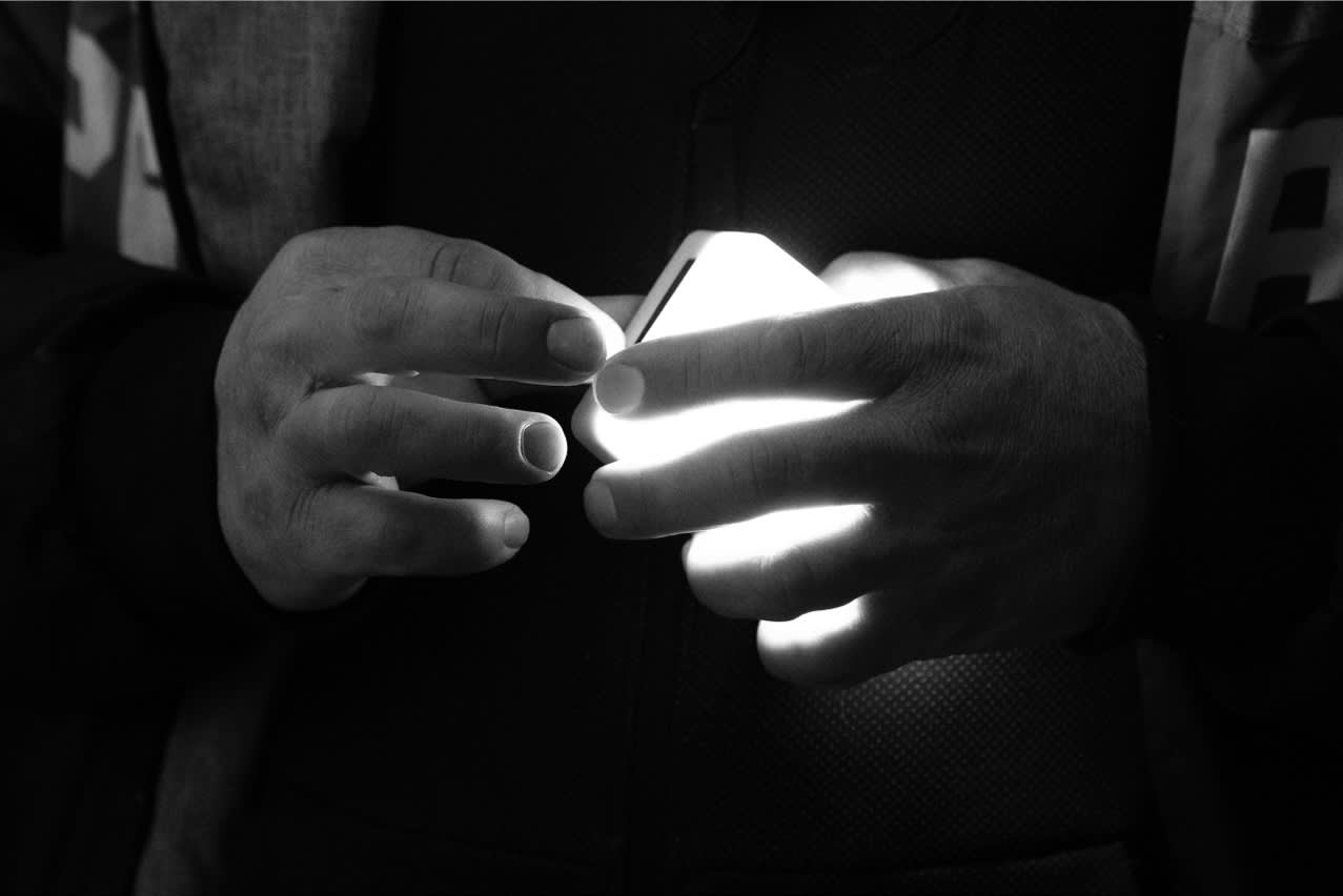 A person’s hands holding a glowing smartphone in the dark, with the light from the screen illuminating their fingers. The background and details of the person are mostly obscured.