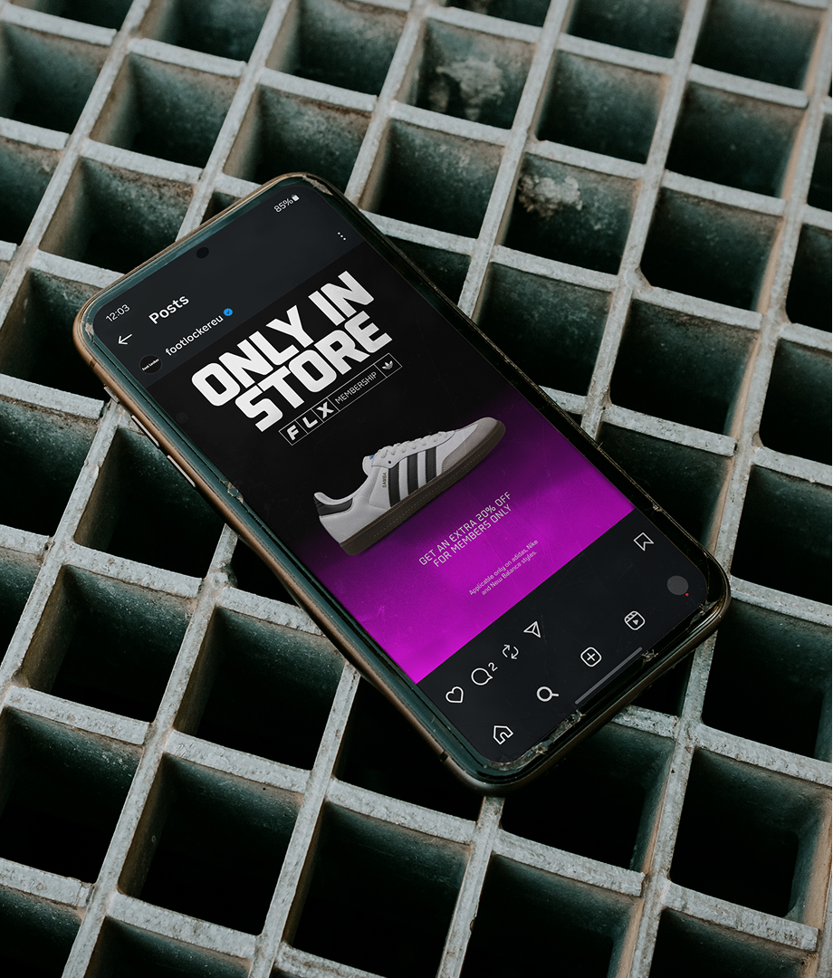A smartphone lying on a metal grate displays an Instagram post featuring a gray Adidas sneaker and the text ONLY IN STORE FLX. The screen has a purple gradient background.
