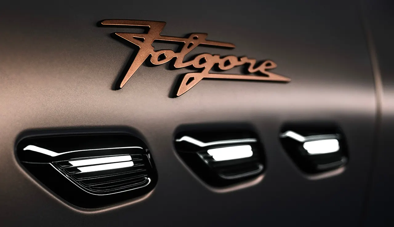 Close-up of a car’s sleek metallic surface featuring the word Folgore in a stylized script above three modern, illuminated air vents.