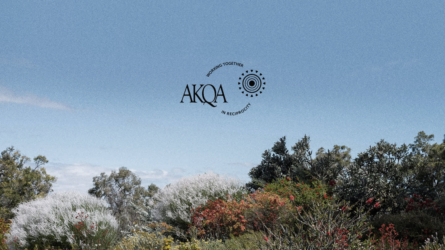 A natural landscape with trees and bushes under a clear blue sky. In the center, the AKQA logo appears with the text “THRIVING TOGETHER IN RECIPROCITY” encircling a circular design.