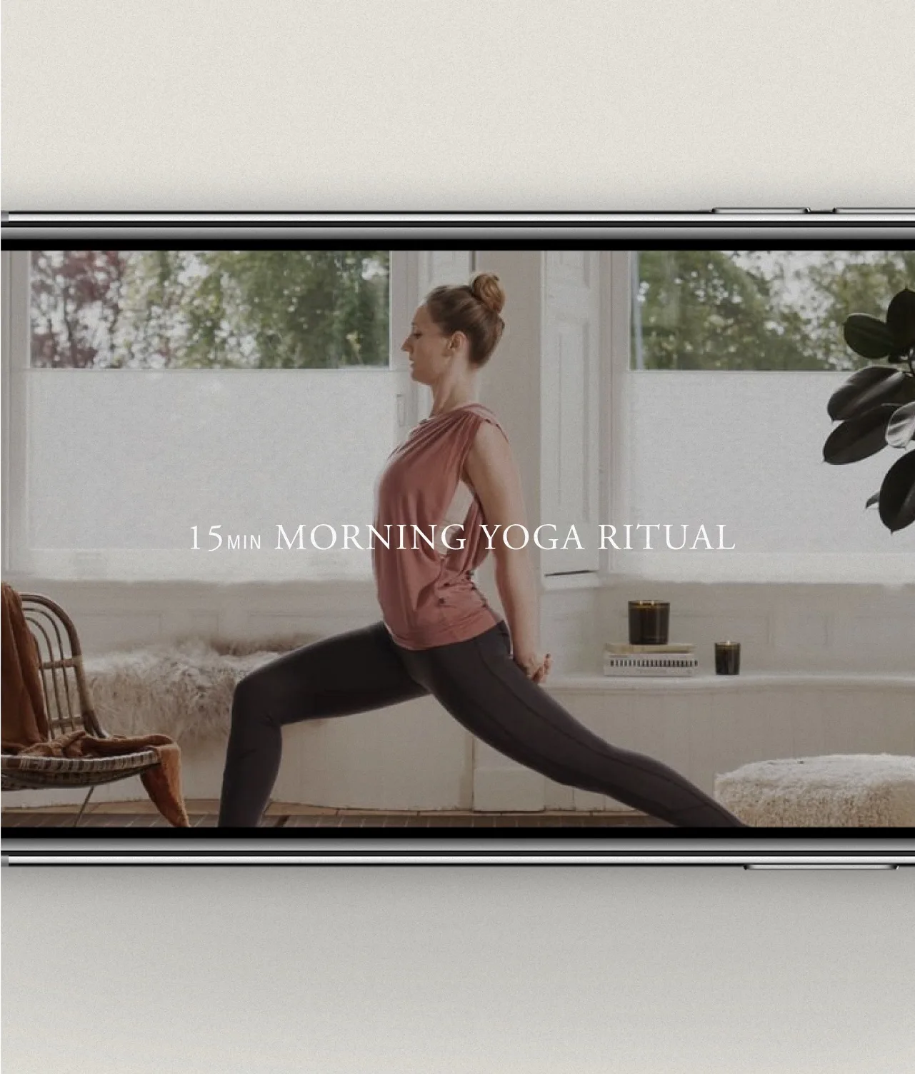A woman practices yoga in a bright living room, performing a lunge pose. Text in the center of the image reads, 15 MIN MORNING YOGA RITUAL. The scene is viewed on a smartphone screen.