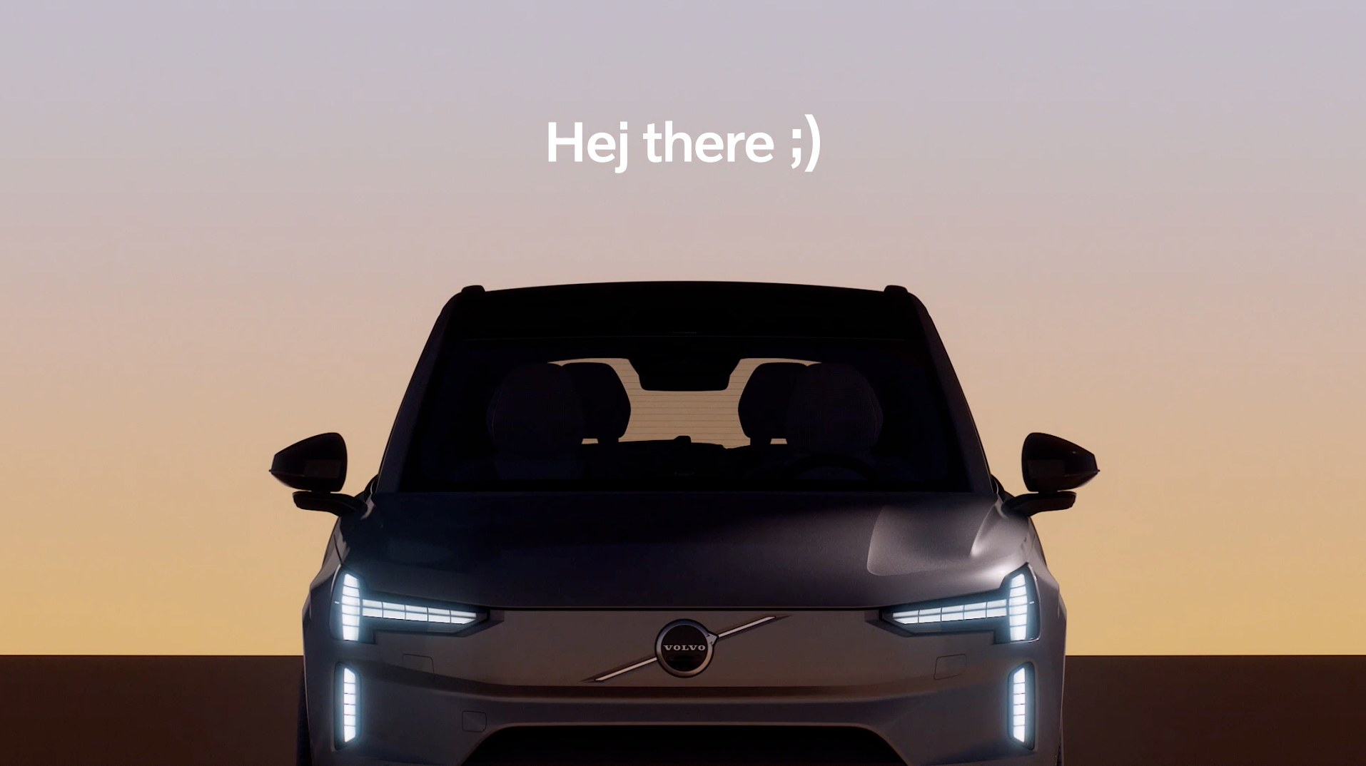 A front-facing black Volvo car is shown against a soft gradient sky at sunset, with the text Hej there ;) displayed above in white font.