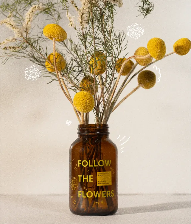 A brown glass jar with yellow billy button flowers and greenery. The jar has FOLLOW THE FLOWERS written in yellow text and is decorated with white doodle flowers on a neutral background.