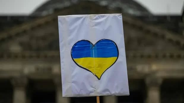 A sign with a heart-shaped design in blue and yellow, resembling the Ukrainian flag, held up in front of a blurred building.