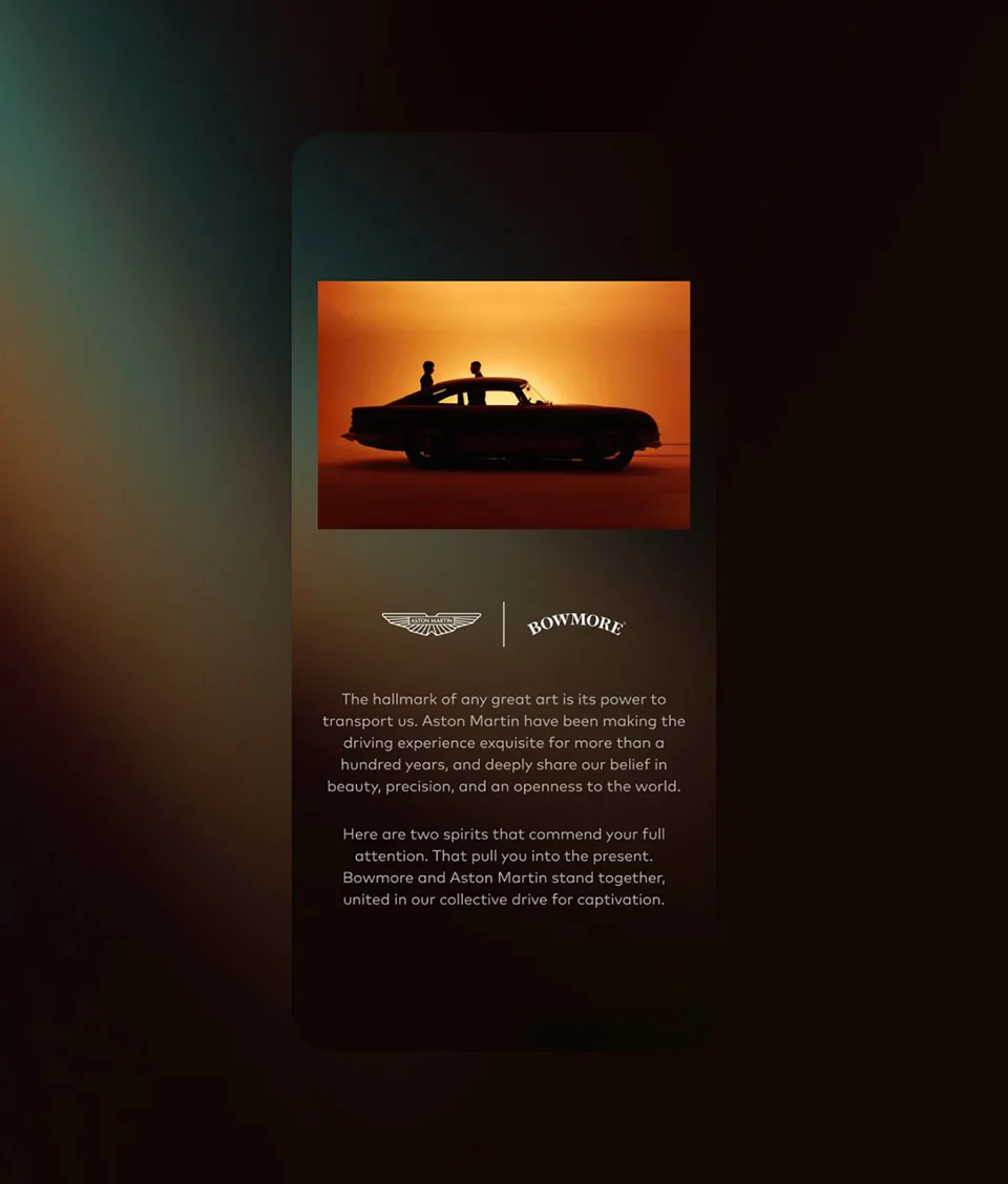 A silhouette of two people standing by a classic Aston Martin car at sunset, with Aston Martin and Bowmore logos and text describing their shared dedication to craftsmanship, beauty, and captivating experiences.