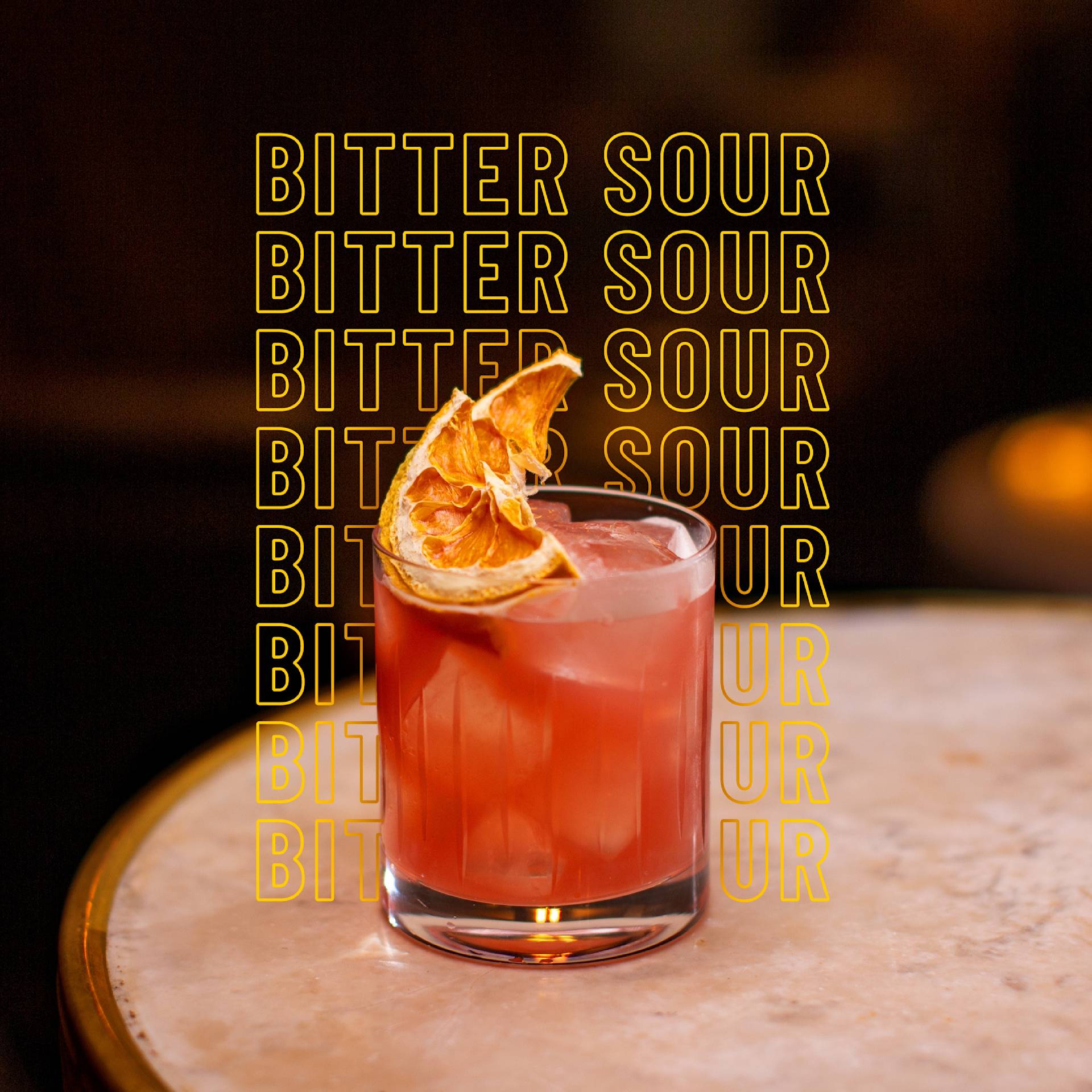 A reddish cocktail garnished with a dried citrus slice sits on a marble table. The words BITTER SOUR are repeated in bold yellow text behind the drink.