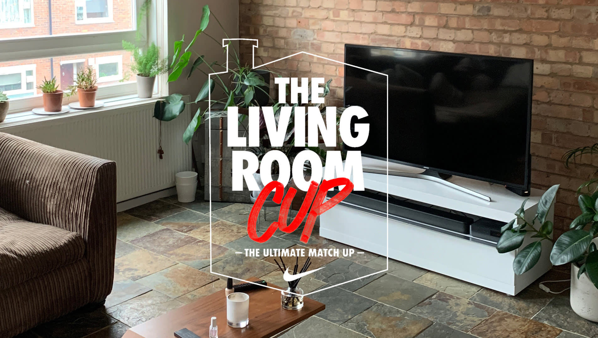 A cozy living room with plants on the windowsill, a brown sofa, a white TV stand with a flat-screen TV, and a coffee table. Text overlay says The Living Room Cup – The Ultimate Match Up.