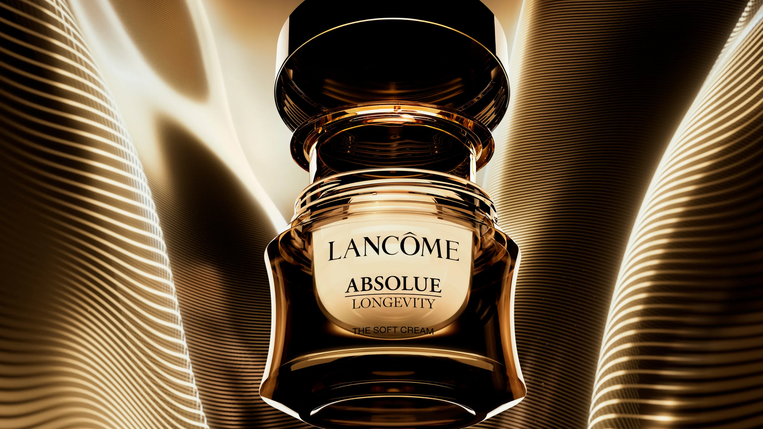 A gold jar of Lancôme Absolue Longevity The Soft Cream is shown open, surrounded by glowing golden light and wavy metallic lines, creating a luxurious and radiant atmosphere.
