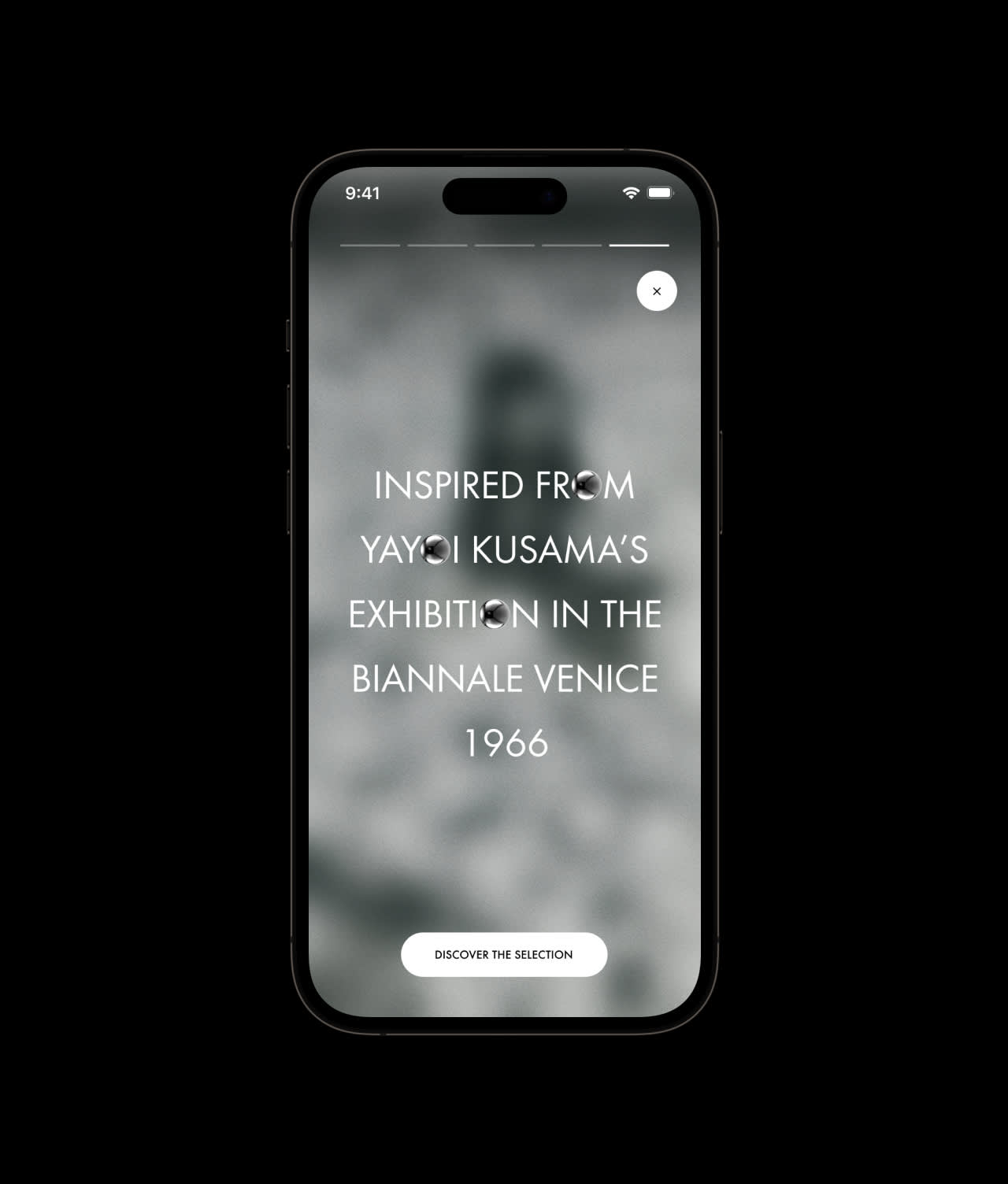 A smartphone screen displays text reading “Inspired by Yayoi Kusama’s exhibition in the Biennale Venice 1966” over a blurred grayscale background, with a button below labeled “Discover the selection.”.