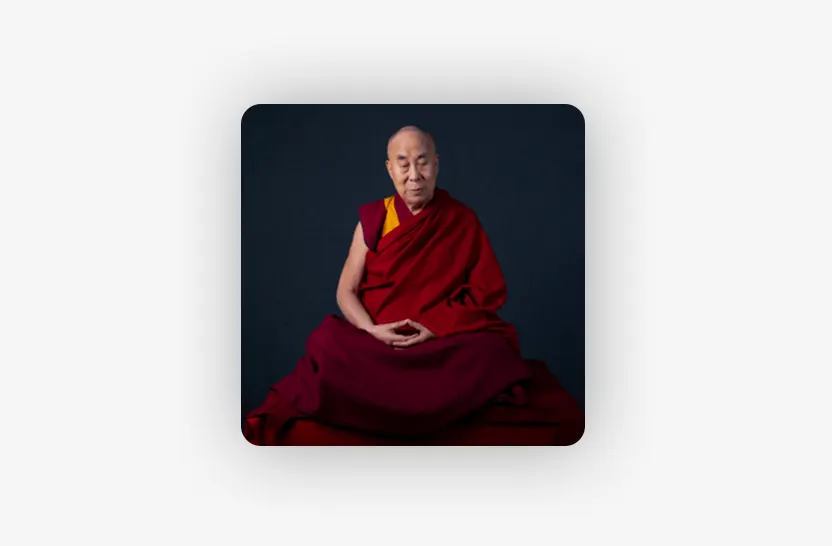 A person in traditional red and yellow monastic robes sits cross-legged against a dark background, with hands resting in their lap in a meditative posture.