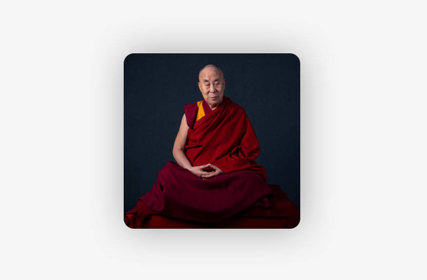 A person in traditional red and yellow monastic robes sits cross-legged against a dark background, with hands resting in their lap in a meditative posture.