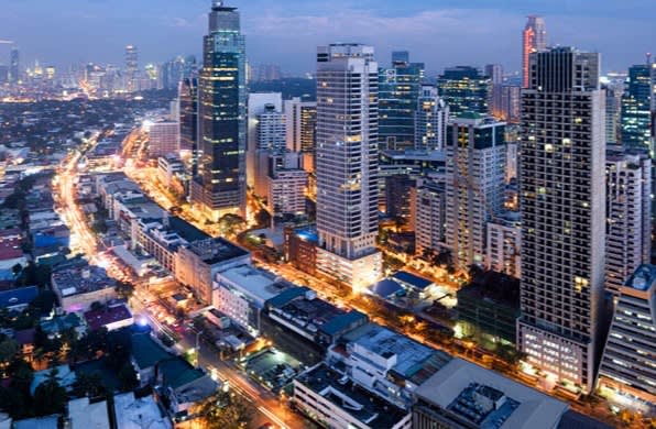 Aerial view of a city skyline at dusk with tall modern buildings, illuminated streets, and a mix of high-rise and low-rise structures. City lights create a vibrant urban atmosphere.