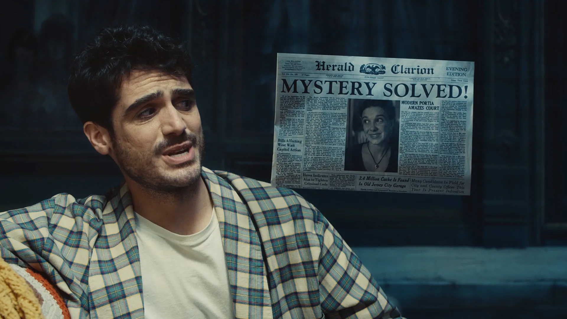 A man in a plaid shirt sits indoors, speaking, while a newspaper with the headline MYSTERY SOLVED! and a photo of a woman appears in the background. The scene is dimly lit.
