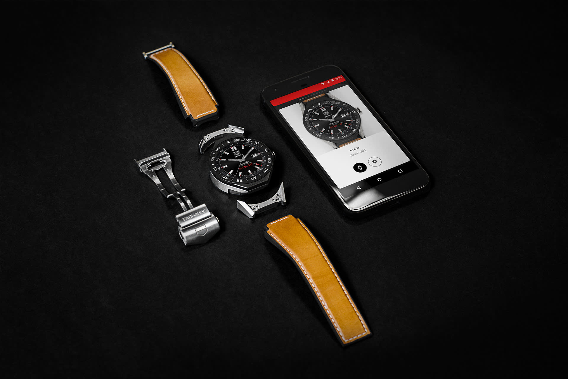 A wristwatch with a black face, two brown leather straps, a metal clasp, and a smartphone displaying the watch are arranged on a black surface.