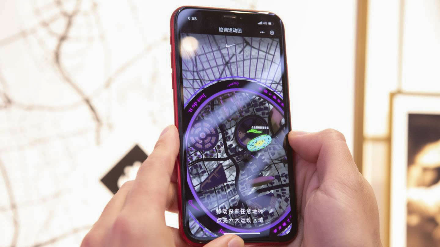 A person holds a smartphone displaying an augmented reality map with Chinese text, featuring colorful graphics and navigational elements overlaid on a city grid.
