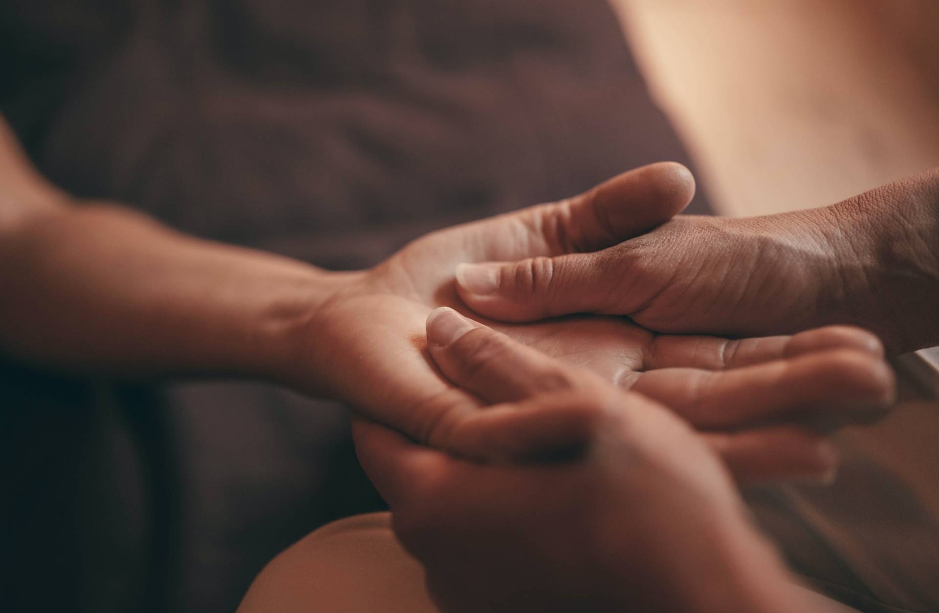 Close-up of one person gently massaging the palm of another persons hand, creating a sense of relaxation and care. The background is softly blurred.
