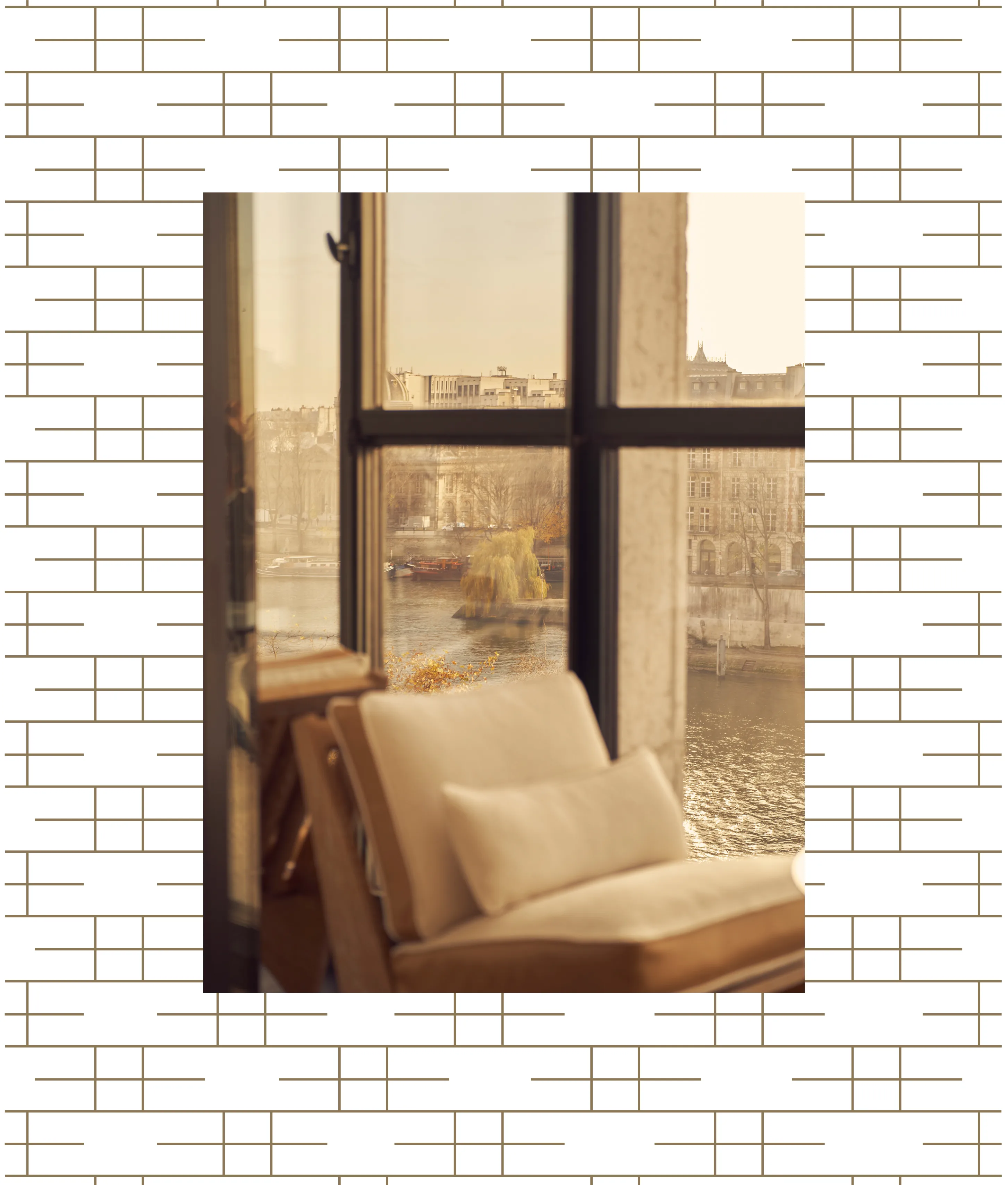 A cozy chair faces large windows overlooking a river and historic buildings, with warm sunlight illuminating the scene. The background features a simple geometric line pattern.