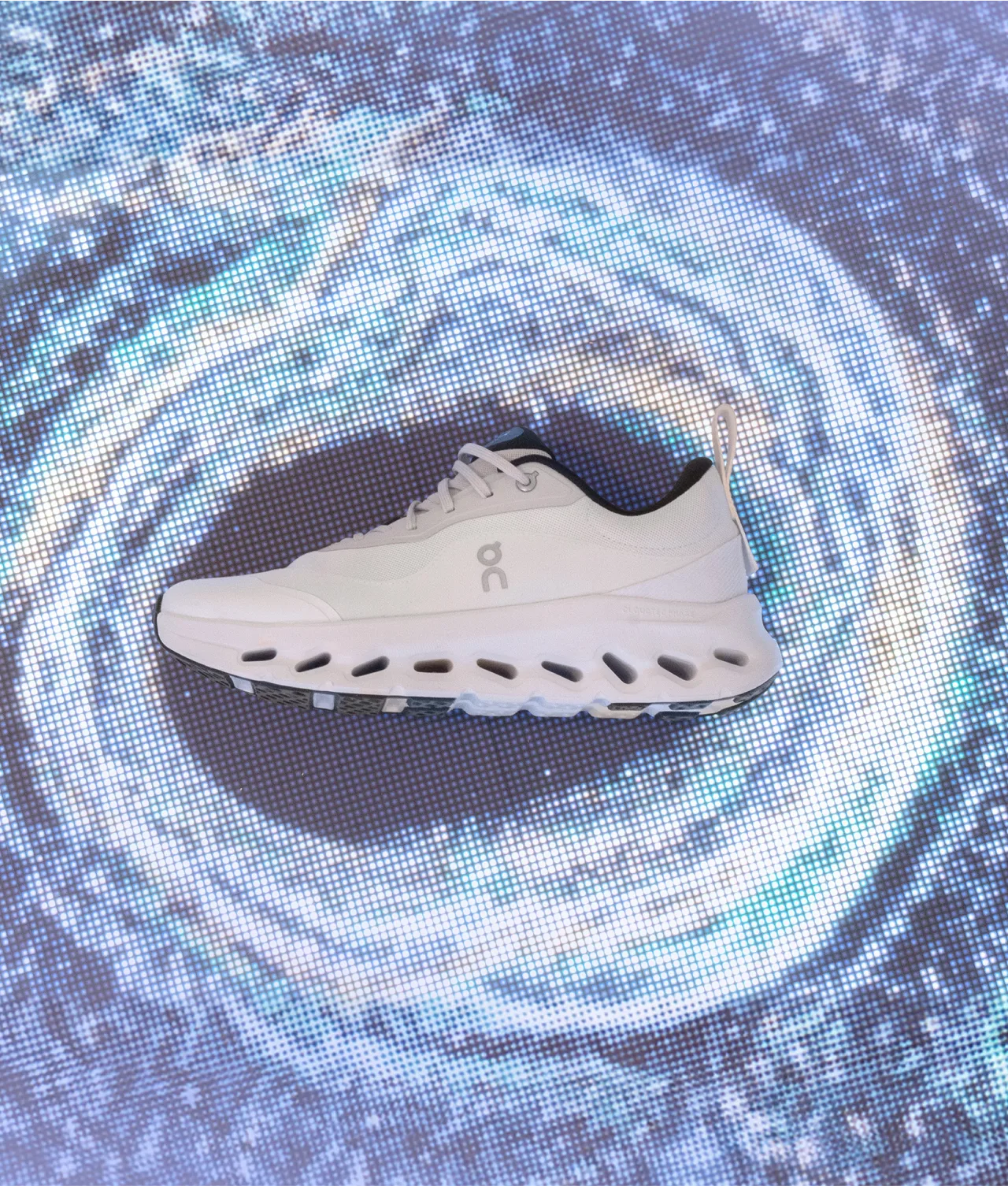 A white athletic shoe with unique cut-out soles is displayed against a swirling blue and white abstract background, resembling a vortex or galaxy.