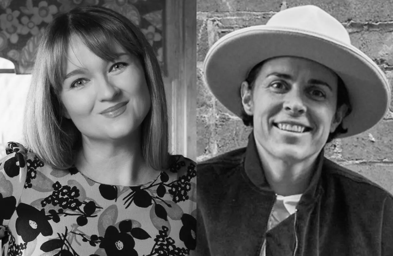A black-and-white photo shows two people side by side; on the left, a smiling woman with straight hair wearing a patterned dress, and on the right, a smiling person in a wide-brimmed hat and jacket standing against a brick wall.