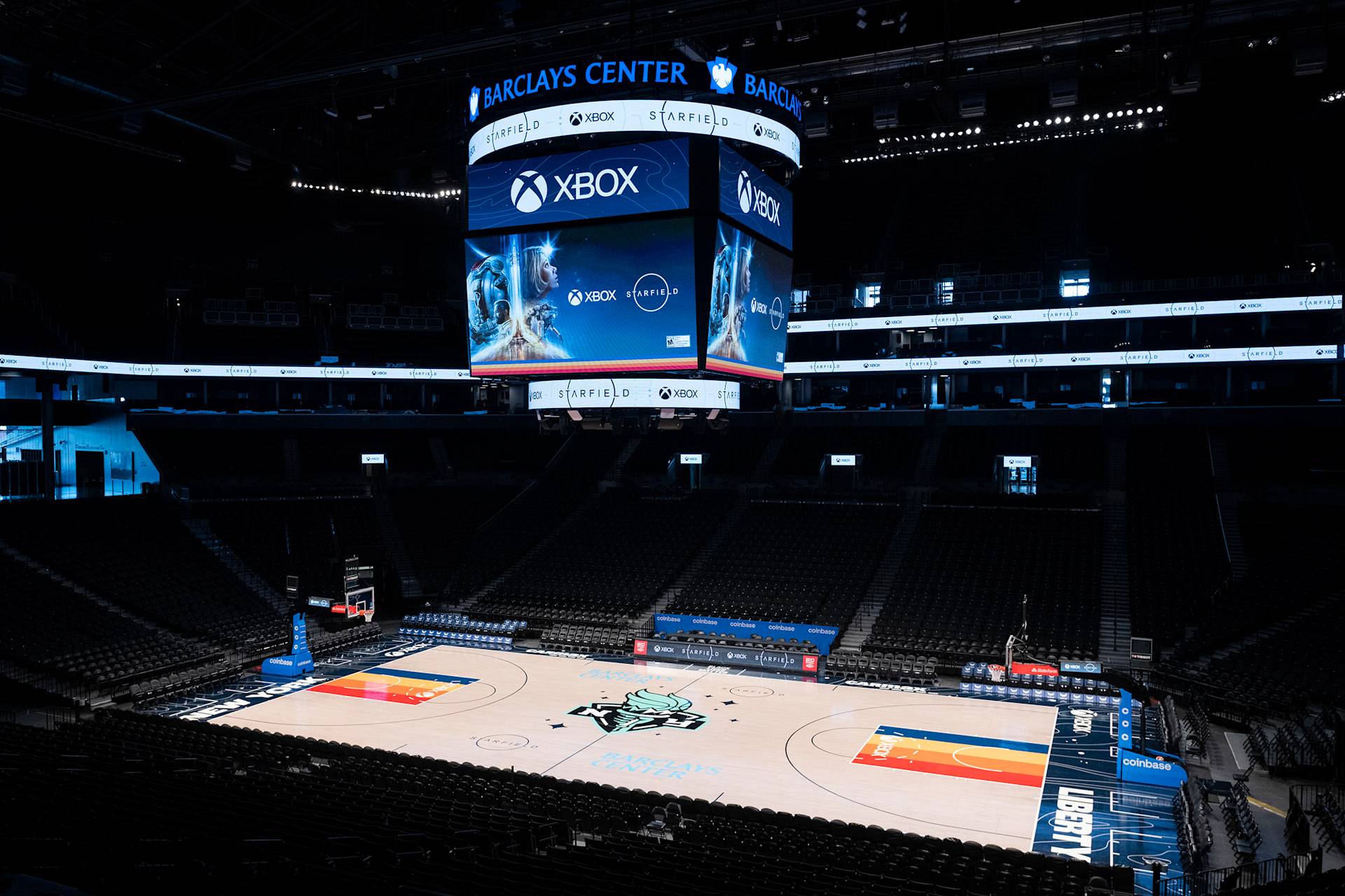 Barclays Center basketball court with empty seats; a large overhead screen displays an Xbox advertisement featuring a video game character, with the New York Liberty logo visible at center court.