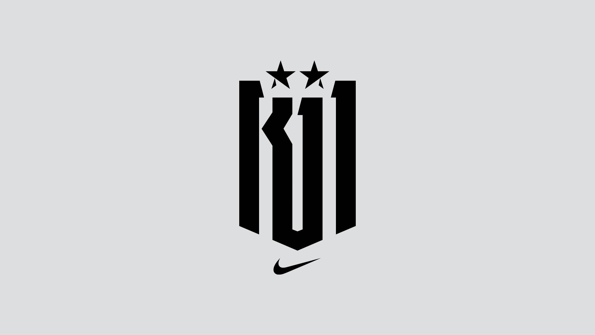 Black geometric logo with two stars above, resembling the number 101 or stylized KU1, on a light gray background. A small black Nike swoosh appears below the main design.