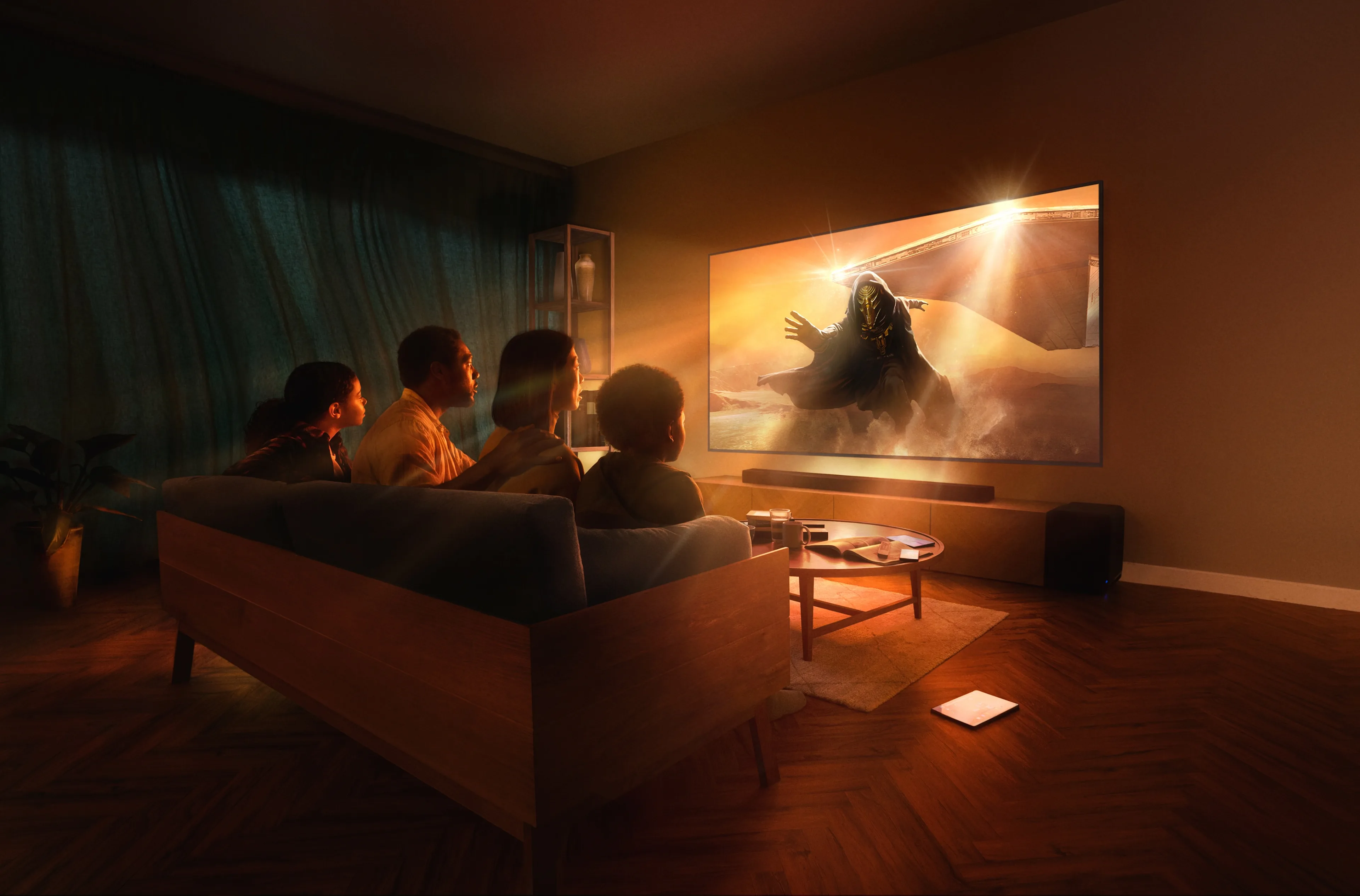 A family of four sits on a couch in a dimly lit living room, watching an action-packed scene on a large wall-mounted TV. Warm light from the screen illuminates their faces and the cozy room.