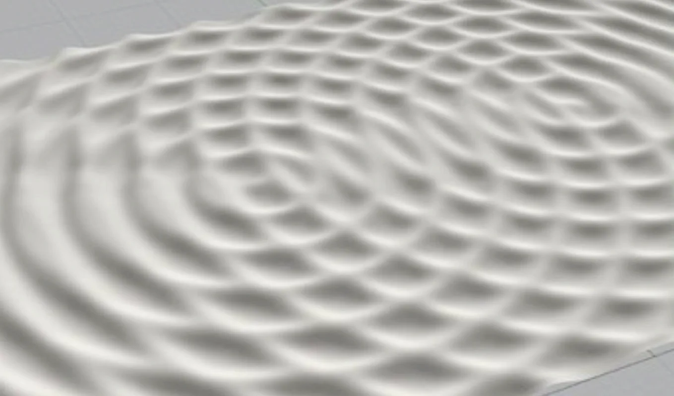 A grayscale image shows overlapping circular wave patterns creating an interference pattern on a smooth surface. The waves form a grid-like arrangement of peaks and troughs.