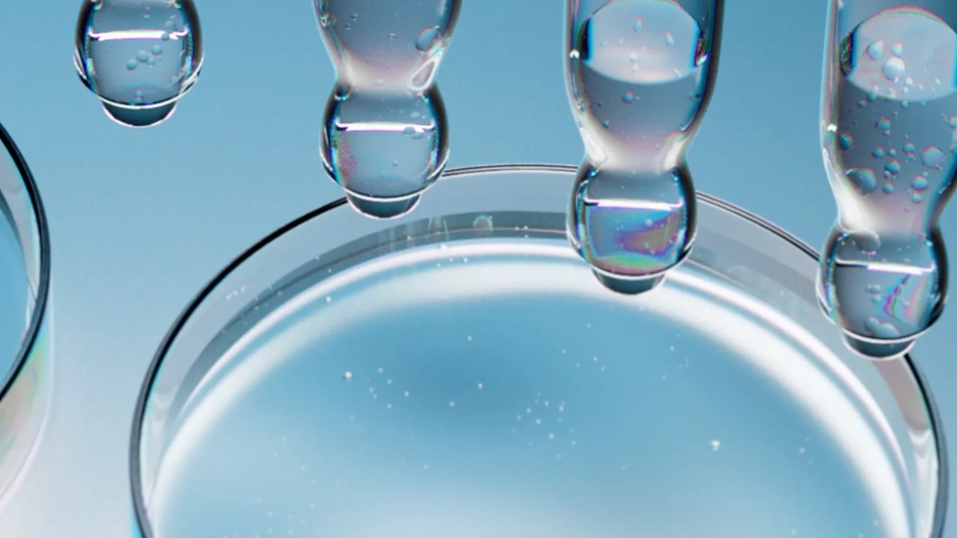 Close-up of several droppers releasing clear liquid into a petri dish against a blue background, with light reflections and small bubbles visible in the liquid.