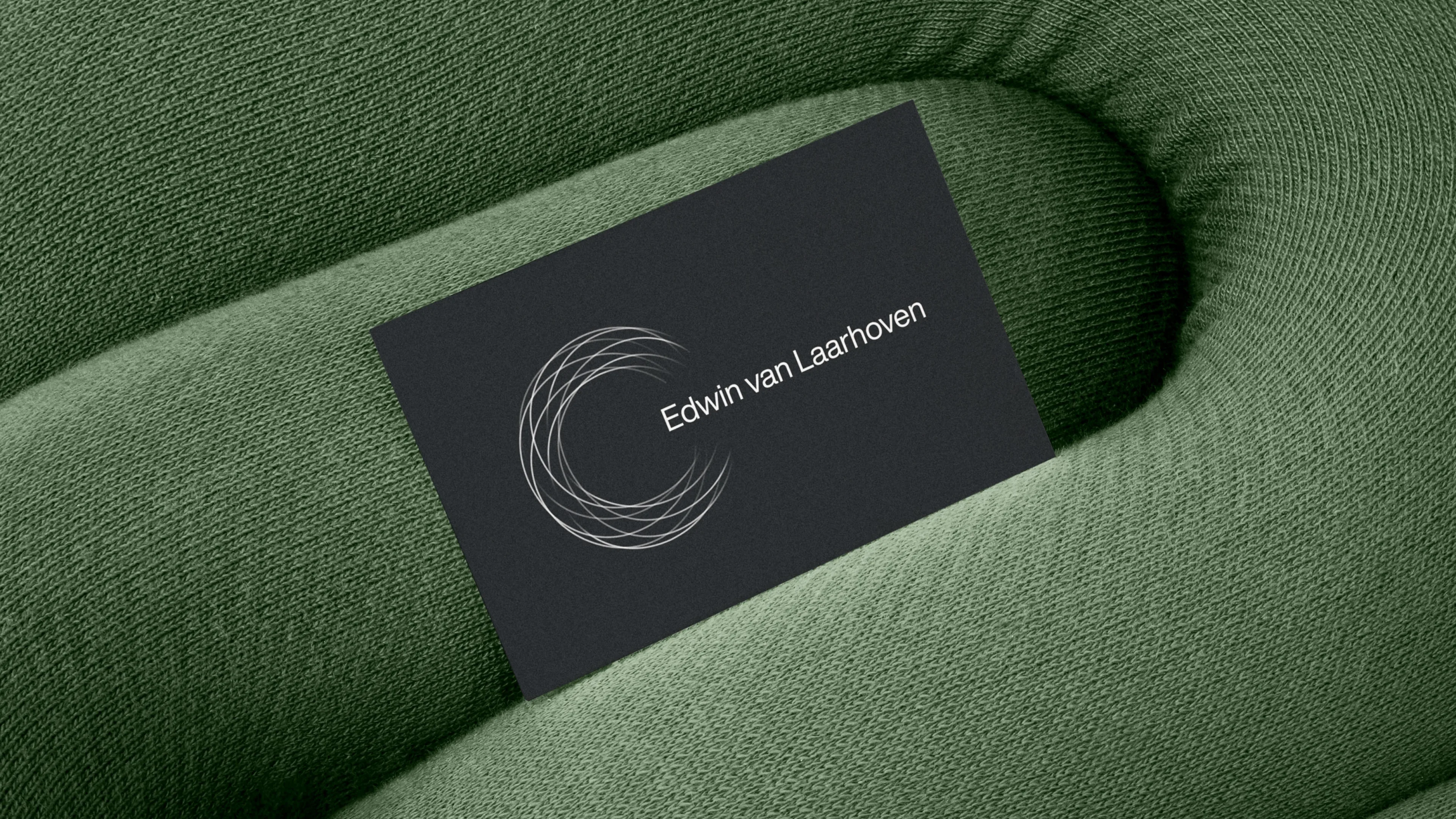 A black business card with a circular line design and the name Edwin van Laarhoven rests on a textured, green fabric surface with curved, padded contours.