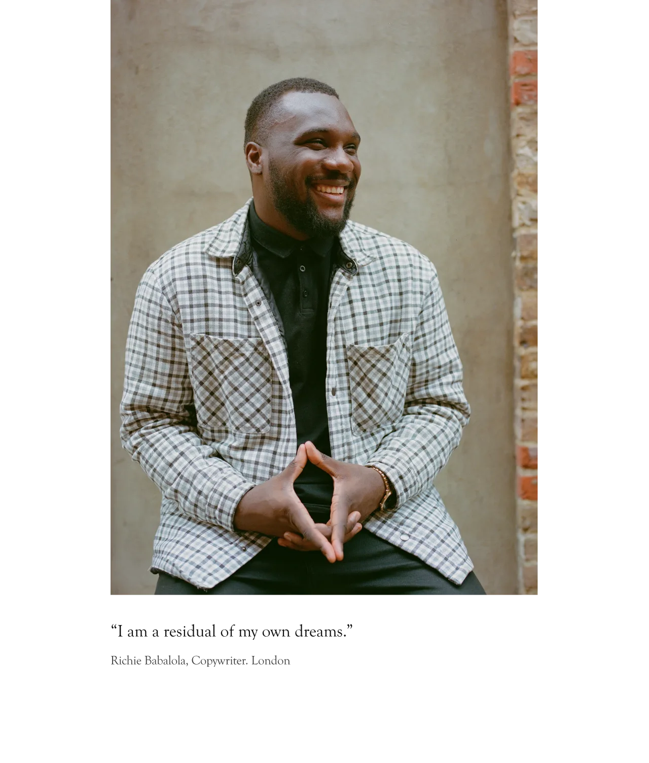 A smiling man sits against a brick wall, wearing a black shirt and a plaid jacket. His hands are clasped in front of him. The caption below reads: “I am a residual of my own dreams.”.