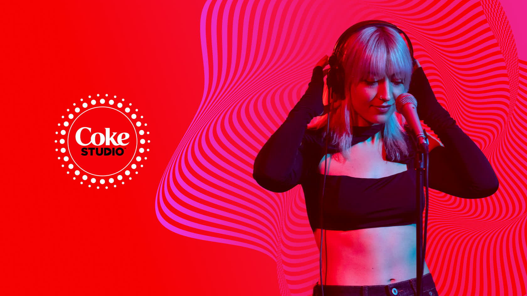 A woman wearing headphones sings into a microphone against a vibrant red and pink background with wavy lines. The Coke Studio logo appears on the left side of the image.